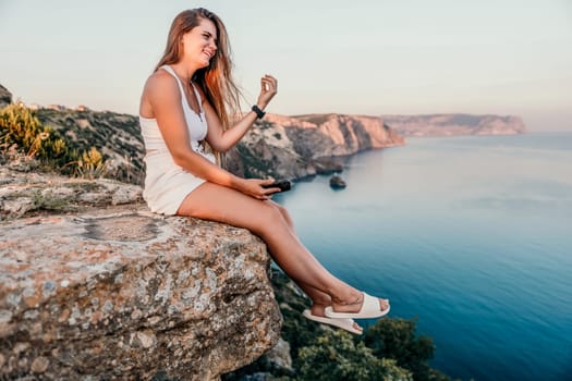 Woman travel sea. Young Happy woman in a long red dress posing on a beach near the sea on background of volcanic rocks, like in Iceland, sharing travel adventure journey