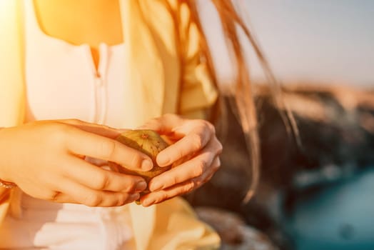 Cutting fig in half with woman hands. A young woman in sunglases eats figs on the beach, near sea. Fresh ripe fig fruit in the hands. Ficus carica, Fig - green-yellow fruit