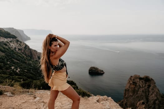 Woman travel sea. Happy tourist taking picture outdoors for memories. Woman traveler looks at the edge of the cliff on the sea bay of mountains, sharing travel adventure journey.