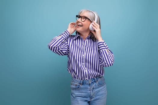 smiling old generation woman with gray hair listening to music with headphones on a bright studio background.