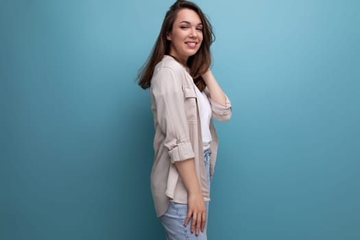 charming young dark-haired lady in informal clothes smiling on blue background.
