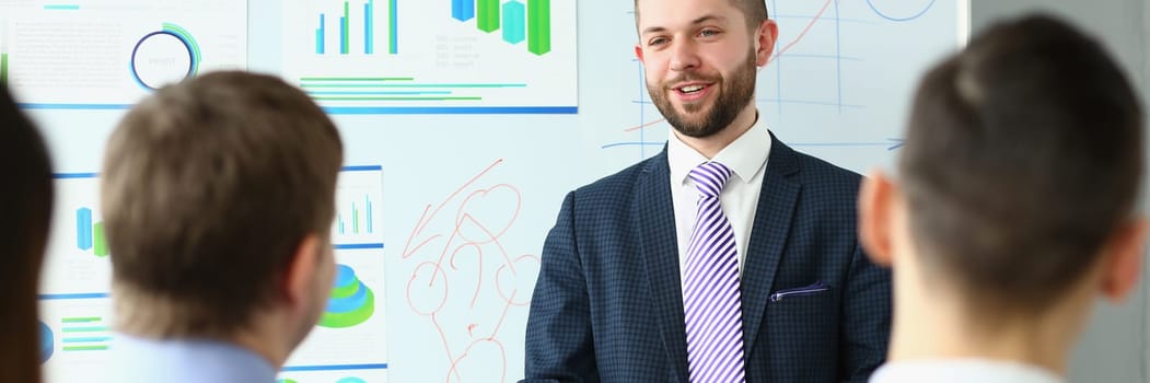 Male business coach speaker in suit makes presentation on white board. Male speaker advising on training and persuading client group employees