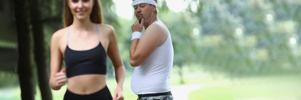 Man emotionally looks at beautiful athletic girl in park. Man jealous of woman athletic body in park