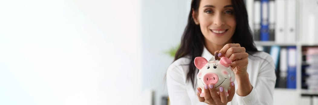 Beautiful smiling woman throws a coin into piggy bank. Accumulation of financial investments and and family savings concept