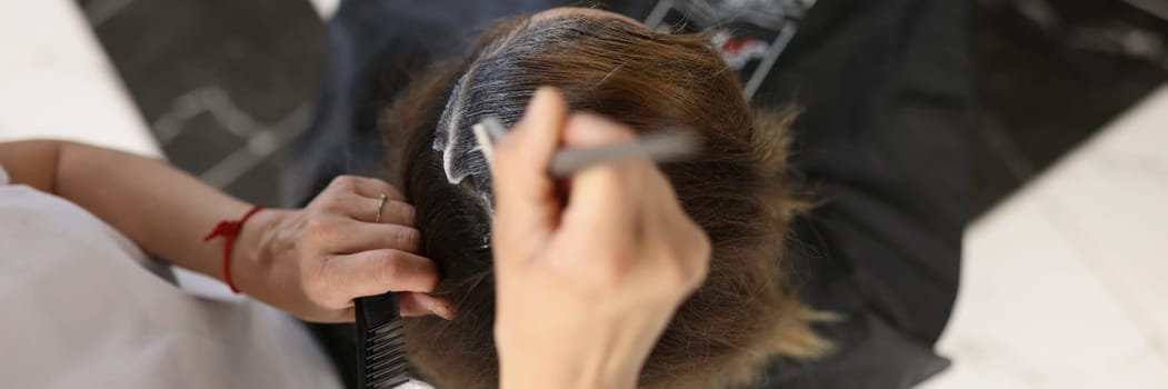 Hairdresser dyes hair of woman in beauty salon. top view. Hair coloring service in barbershop concept