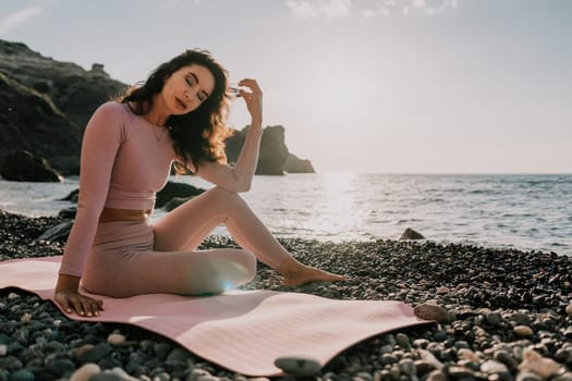 Young woman with black hair, fitness instructor in pink sports leggings and tops, doing pilates on yoga mat with magic pilates ring by the sea on the beach. Female fitness daily yoga concept