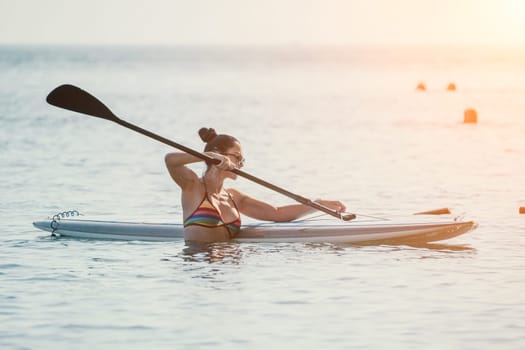 Sea woman sup. Silhouette of happy middle aged woman in rainbow bikini, surfing on SUP board, confident paddling through water surface. Idyllic sunset. Active lifestyle at sea or river