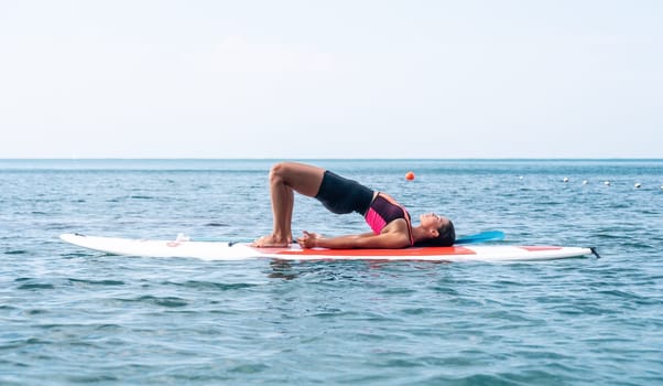 Woman sup yoga. Happy young sporty woman practising yoga pilates on paddle sup surfboard. Female stretching doing workout on sea water. Modern individual female outdoor summer sport activity