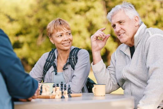 Senior couple playing chess in nature after a wellness, fresh air and health walk in a garden. Happy, smile and elderly people talking, bonding and enjoying a board game together in a green park