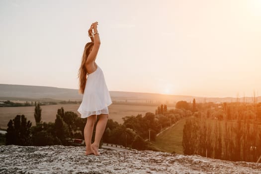 Romantic beautiful bride in white dress posing with sea and mountains in background. Stylish bride standing back on beautiful landscape of sea and mountains on sunset