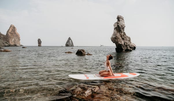 Woman sup yoga. Middle age sporty woman practising yoga pilates on paddle sup surfboard. Female stretching doing workout on sea water. Modern individual hipster outdoor summer sport activity