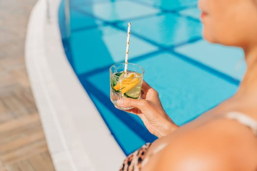 Close up of mature adult woman holding cocktail and relaxing near the pool. Beautiful elegant caucasian senior woman drink lemonade cocktail enjoying summer vacation.