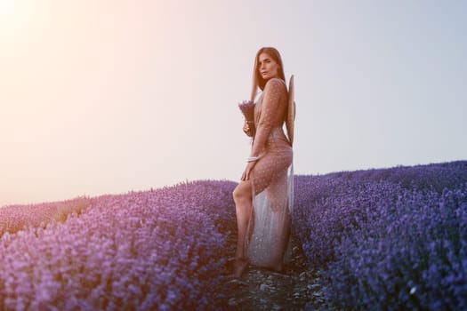 Close up portrait of young beautiful woman in a white dress and a hat is walking in the lavender field and smelling lavender bouquet.