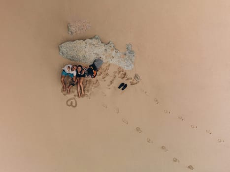 Aerial top view of a young couple enjoying the beach, sitting and lying down on the sand.