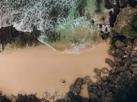 Aerial top view of aptivating beach with rocky foreground, crashing waves, and a reflective body of water. Moody atmosphere, close-ups of rocks.