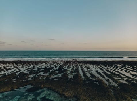 Sunset stone serene beach with clear blue water and shoreline. Waves crash against the beach