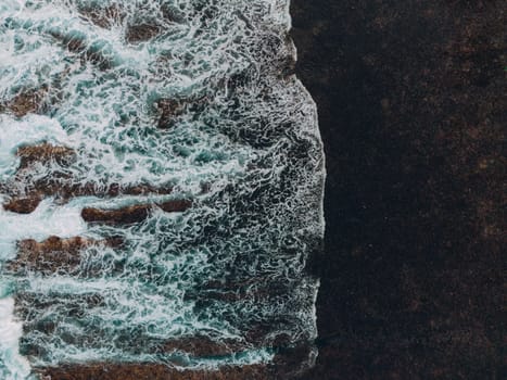 Aerial top view of waves crashing against stone rocks in the ocean wallpaper style