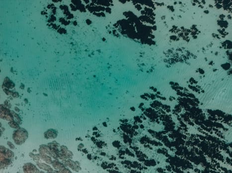 Aerial top view of a breathtaking aerial view of teal and black water with rocks and a black blob