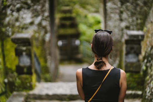 Close up shot of back view of young lady with balinese temple background. Tourist woman visiting Pura Gunung Kawi temple