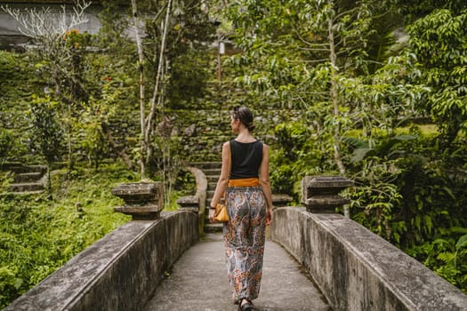 Young stylish girl walking on Pura Gunung Kawi temple bridge. Ancient rocky monument attraction, holy balian royal tombs