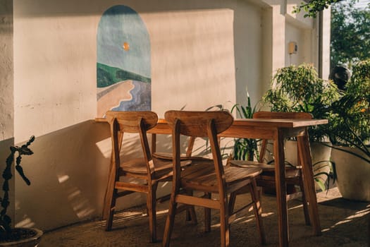 Wooden table with chairs at white wall with decorative painting. Outdoor summer table in tropical garden