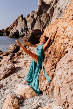 Woman green dress sea. Woman in a long mint dress posing on a beach with rocks on sunny day. Girl on the nature on blue sky background