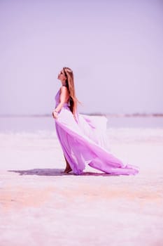 Woman pink salt lake. Against the backdrop of a pink salt lake, a woman in a long pink dress takes a leisurely stroll along the white, salty shore, capturing a wanderlust moment