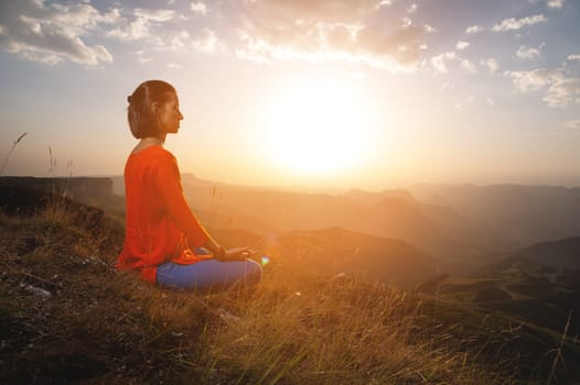 A woman practices yoga and meditates on a mountain. Side view of a yogi practicing in the mountains at dawn in the rays of the sun receiving the energy of a new day.