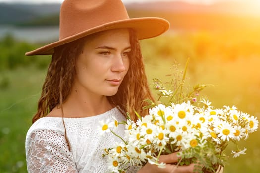 A middle-aged woman in a white dress and brown hat holds a large bouquet of daisies in her hands. Wildflowers for congratulations.