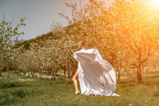 Woman white dress park. A woman in a white dress runs through a blossoming cherry orchard. The long dress flies to the sides, the bride runs rejoicing in life