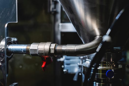 Stainless steel tank with pipe outlet and tap, surrounded by pneumatic equipment and pipes.