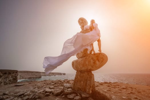 Woman sky stone. Lady stands on stone sculpture with ocean view. She is dressed in a white long dress, against the backdrop of the sea and sky. The dress develops in the wind