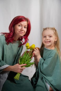 Amazing pretty mother and daughter having fun with flowers in 8 March or in Mother's day. Red haired mom and small little blonde girl having lovely free time on white background in studio