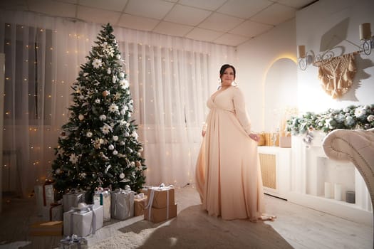 Owerweight elegant Woman at Christmas room. Fat plumb pretty girl in a beautiful dress for a holiday. Buxom female model posing alone in New year sudio