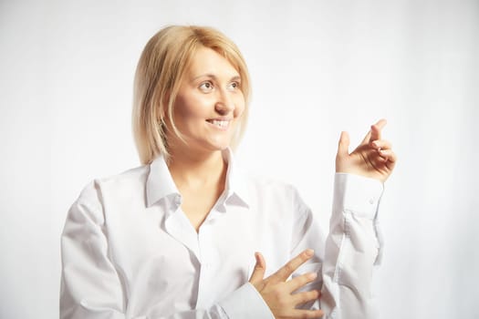 Portrait of a pretty blonde smiling woman posing on white background and pointing somewhere. Happy girl model in white shirt posing in studio. Copy space