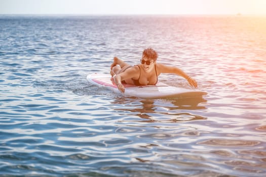 Woman sup sea travel. Sports girl on a surfboard in the sea on a sunny summer day. In a black bathing suit, he sits on a sapa in the sea. Rest on the sea