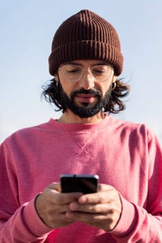stylish bearded young man in pink jersey texting on his smart phone, concept of modern lifestyle and technology of communication