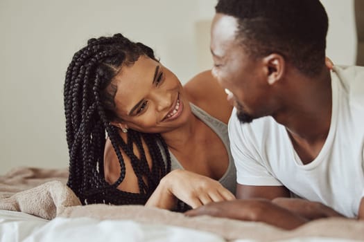 Black couple, love and home bedroom bonding while happy together on a bed at home, apartment or hotel for honeymoon. Young man and woman talking while in a happy marriage with communication and care.