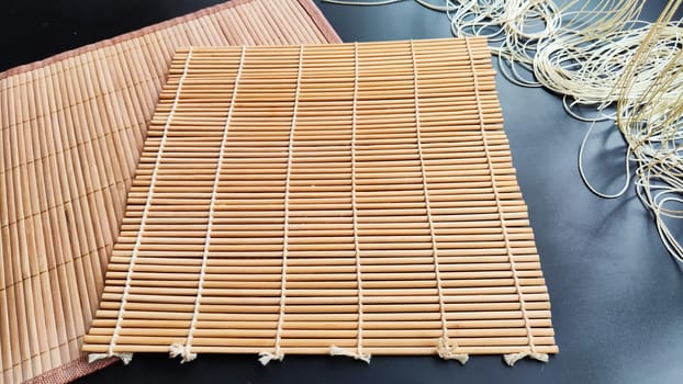 Big rectangular and small square Asian bamboo mats and napkins from yellow bamboo on black surface. Background, texture, frame, copy space, location for the photo shoot