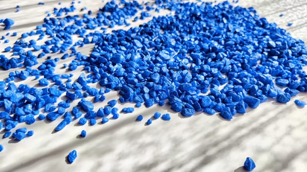 Blue painted small pebble on the surface of table under sunlight. Abstract background, texture, frame, and copy space. Supplies for crafting and handmade.