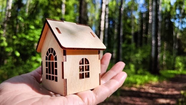 Small wooden toy house on palm of woman hand on natural background. symbol and concept of care of family and buying, selling, donating of eco friendly home. copy space. close-up. soft selective focus