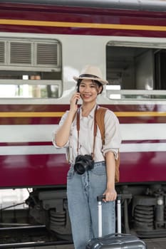 Traveler young asian woman talking on cell phone at terminal train station. Happy tourist travel by train. woman Backpacker arrival at platform railway. Freedom trip on vacation time holiday weekend.