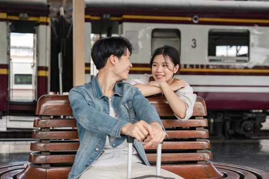 Young couple sitting on wooden bench at train station. Couple sitting waiting for the train at platform.