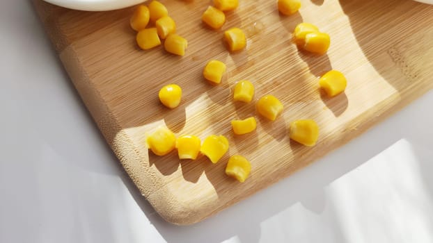 Lot of pieces of canned yellow corn on plate which is on wooden bamboo cutting board on white background. Concept of cooking and delicious healthy food