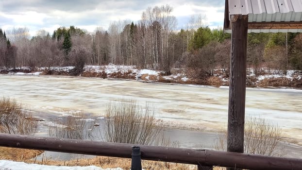 Small river with water under wet swollen ice ready for ice drift, sky with low dark clouds and forest in background in early spring afternoon. Nature landscape during trip to the rural countryside