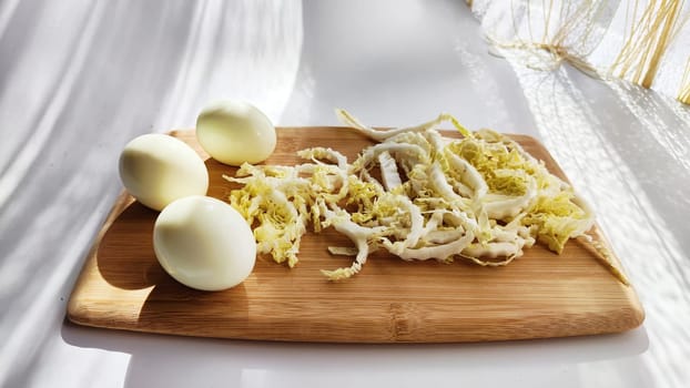 Chopped Peking cabbage and peeled eggs on cutting board as background. Cooking a healthy eco-friendly salad from natural products. Copy space and place for text