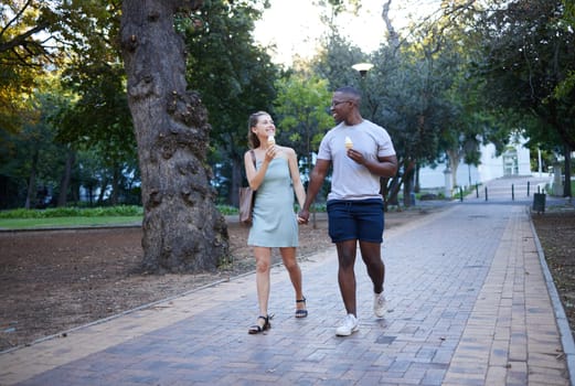 Couple on date in park, ice cream and holding hands outdoor, love and commitment in relationship. Romance in nature, black man and woman eat dessert for quality time together, trust and interracial.