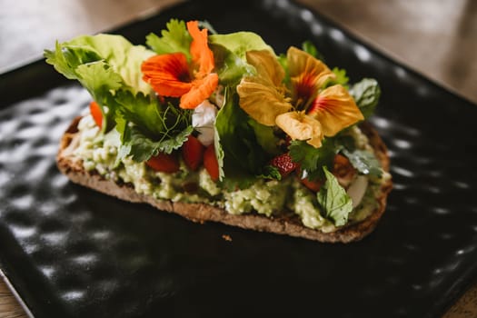 Close up shot of avocado bruschetta with tomatoes and herbs. Morning tropical breakfast toast on black plate