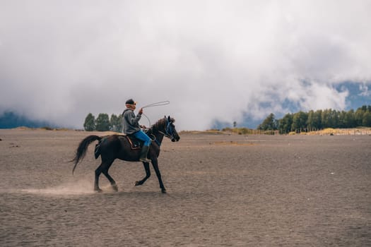 Bromo mount unrecognized horseman riding in the savanna desert. Horse trip in Semeru National Park Indonesia