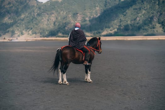 Bromo mount unrecognized horseman riding in the savanna desert. Horse trip in Semeru National Park Indonesia